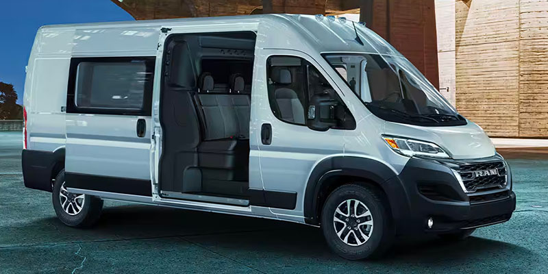 A silver 2025 Ram ProMaster van parked, showing an open side door and spacious interior.