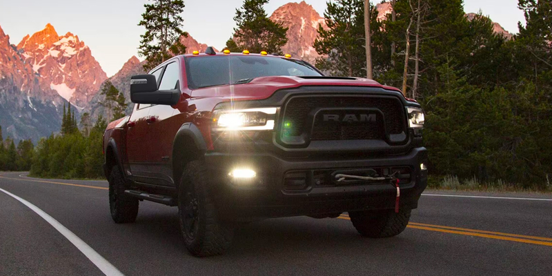 A rugged red RAM 2500 pickup truck driving through a scenic mountain road.