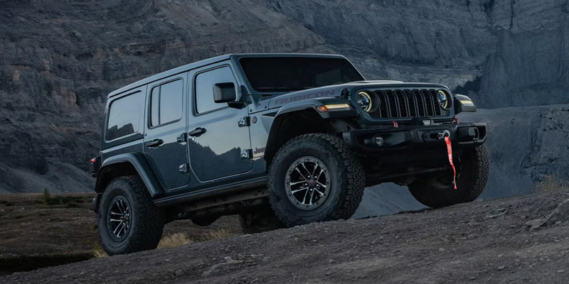 Gray Jeep Wrangler Rubicon climbing a rocky off-road trail with rugged terrain in the background.
