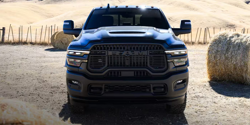 Front view of a Ram pickup truck parked on a dirt road in a rural field with hay bales.