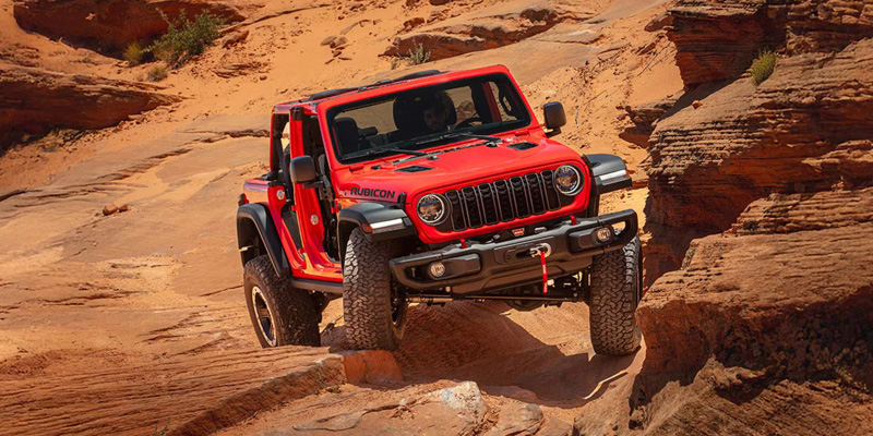 Red Jeep Wrangler navigating a rocky off-road canyon trail.