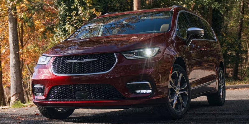 Red Chrysler Pacifica minivan parked on a tree-lined road.