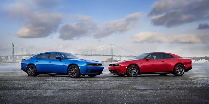 Blue and red 2026 Dodge Charger models parked facing each other with a bridge in the background.