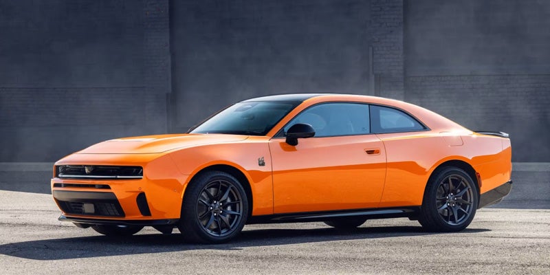 Orange 2026 Dodge Charger parked in side profile against a dark wall.