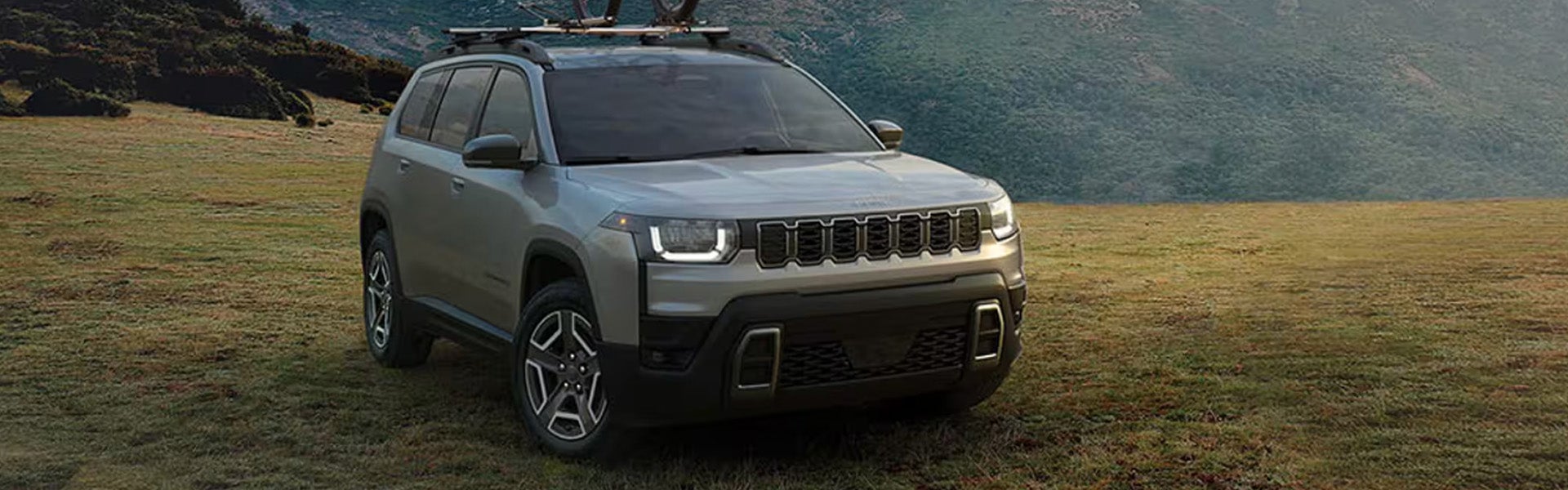 2026 Jeep Cherokee parked on grass near a lake with its headlights illuminated.
