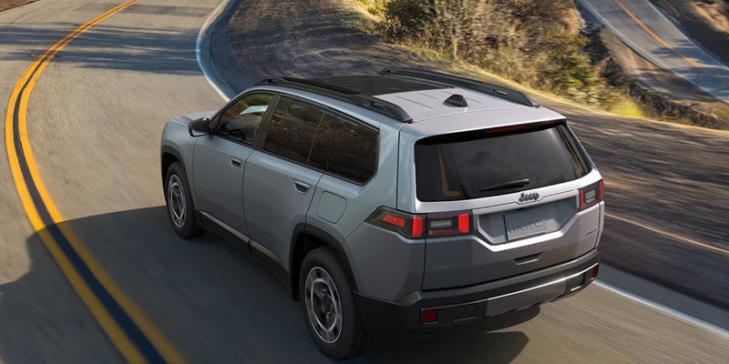 Gray 2026 Jeep Cherokee shown from a rear three-quarter angle while driving on a curved road.