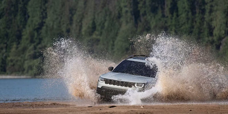 White 2026 Jeep Cherokee driving through shallow water with large splashes on both sides.