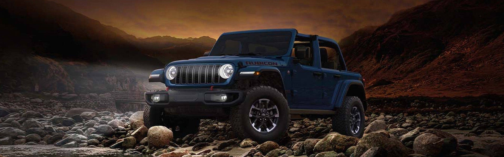 2026 Jeep Wrangler parked off-road on rocky terrain at sunset.