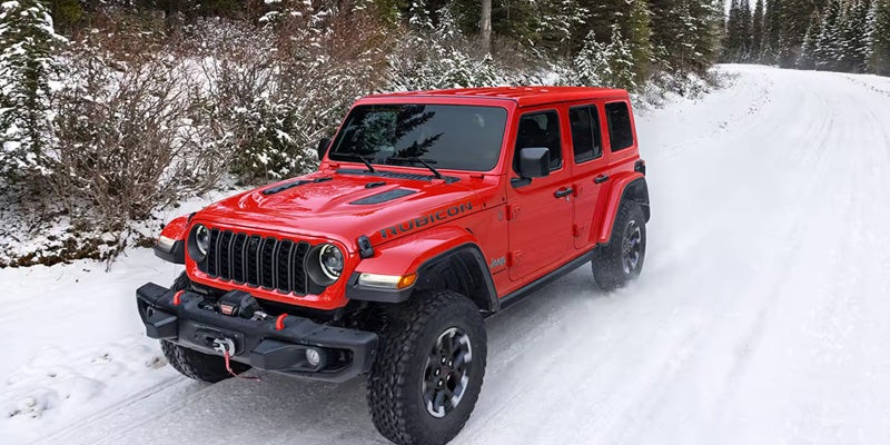 Red 2026 Jeep Wrangler driving in snowy conditions.