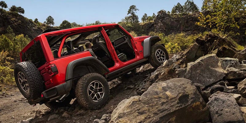 Red 2026 Jeep Wrangler rock crawling with doors off.